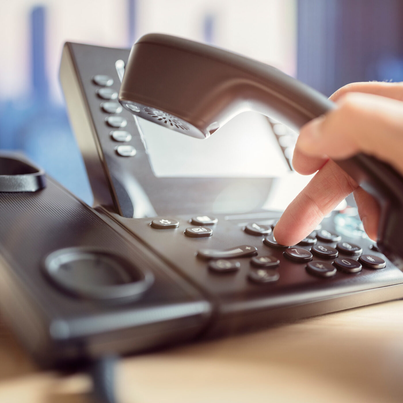 Eine Hand mit Telefonhörer in der Hand, wählt eine Rufnummer am Telefon.